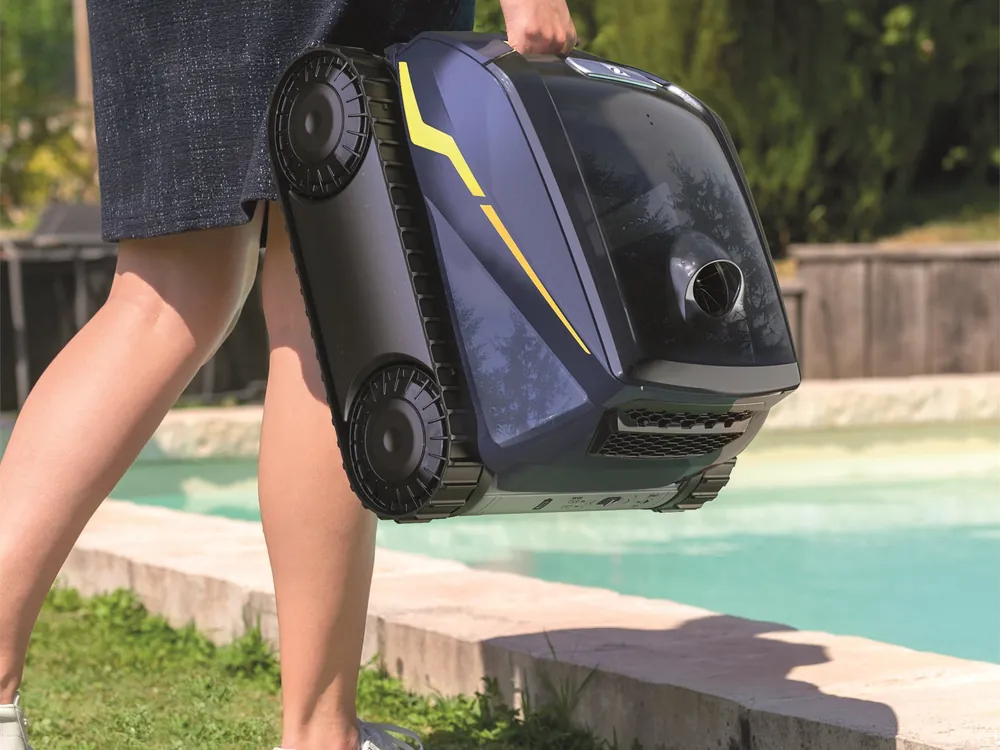 The cleaner carried across the lawn by its top handle, no cable trailing