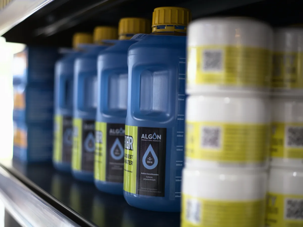 Bottles of pool chemical lined up along a shop shelf